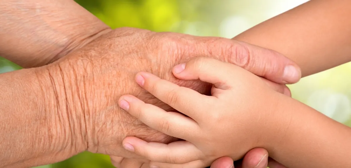 An older adult's hands hold a child's hands